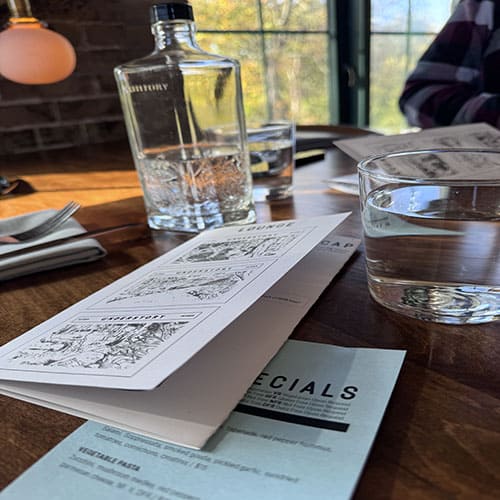 Understory water glass and menu, view out the window with a blue sky and fall trees